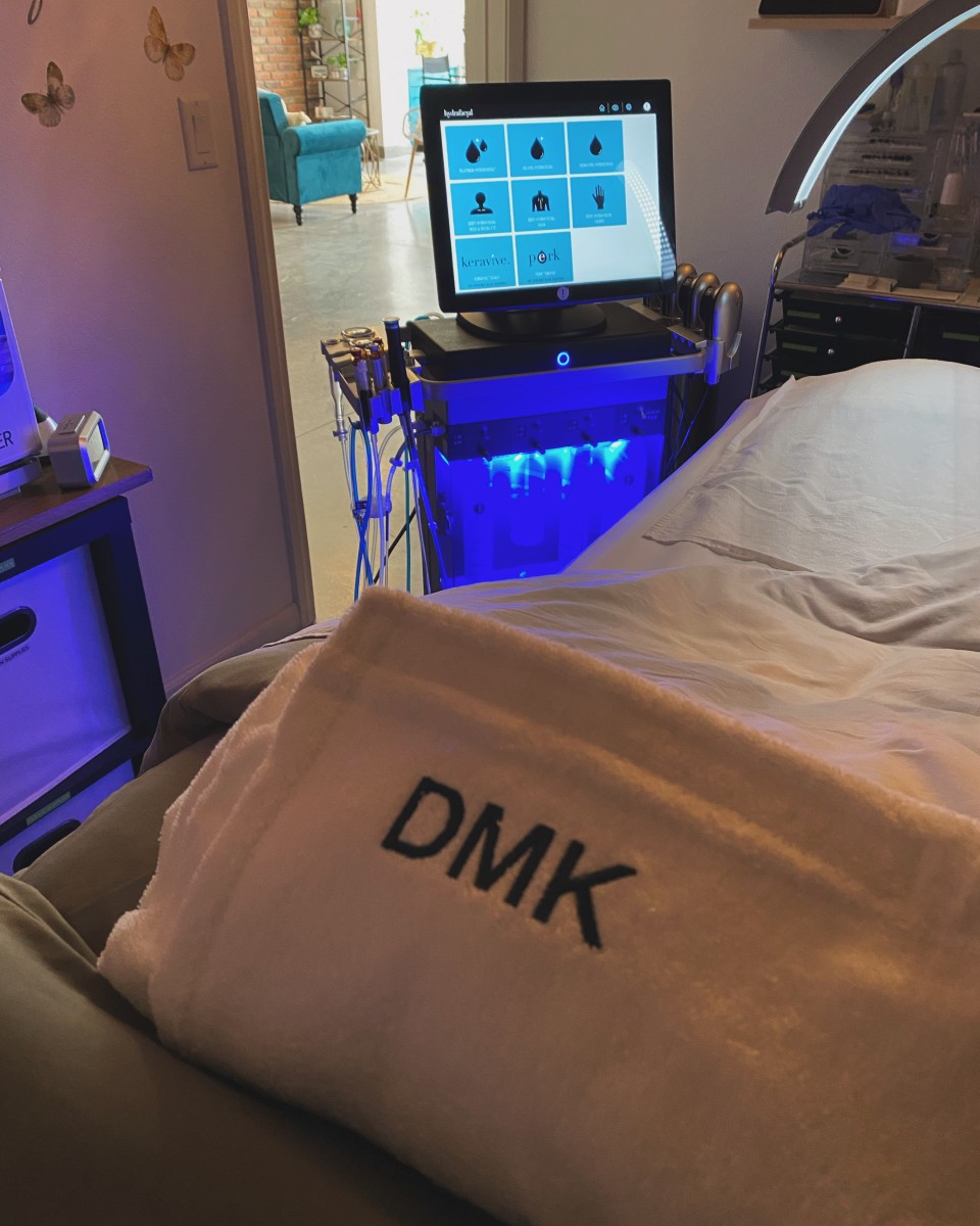 An image that shows a towel that says the brand DMK with a hydrafacial machine in the back.