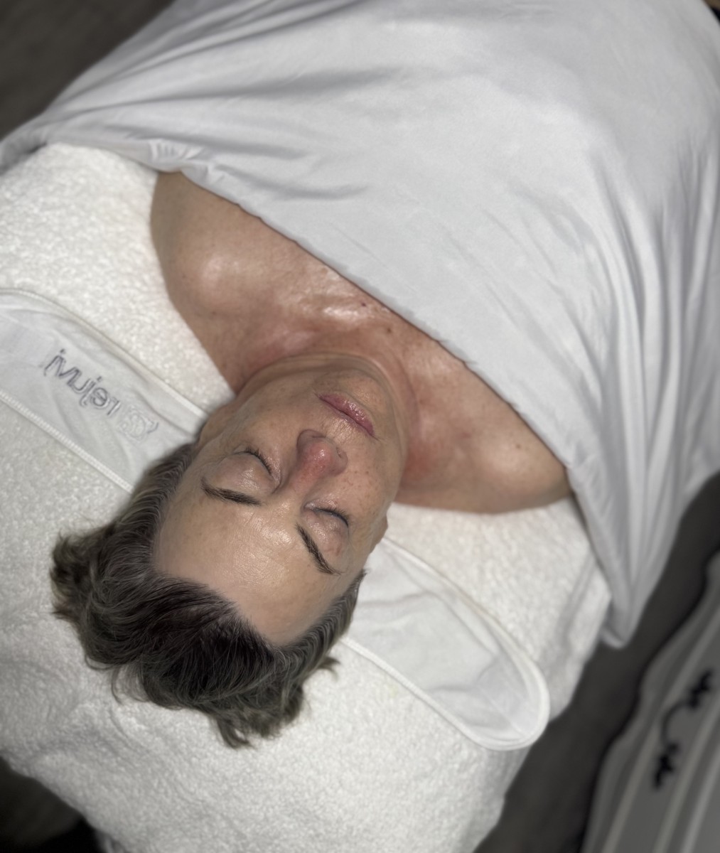 A woman laying on a bed with her eyes closed to get a professional facial service.